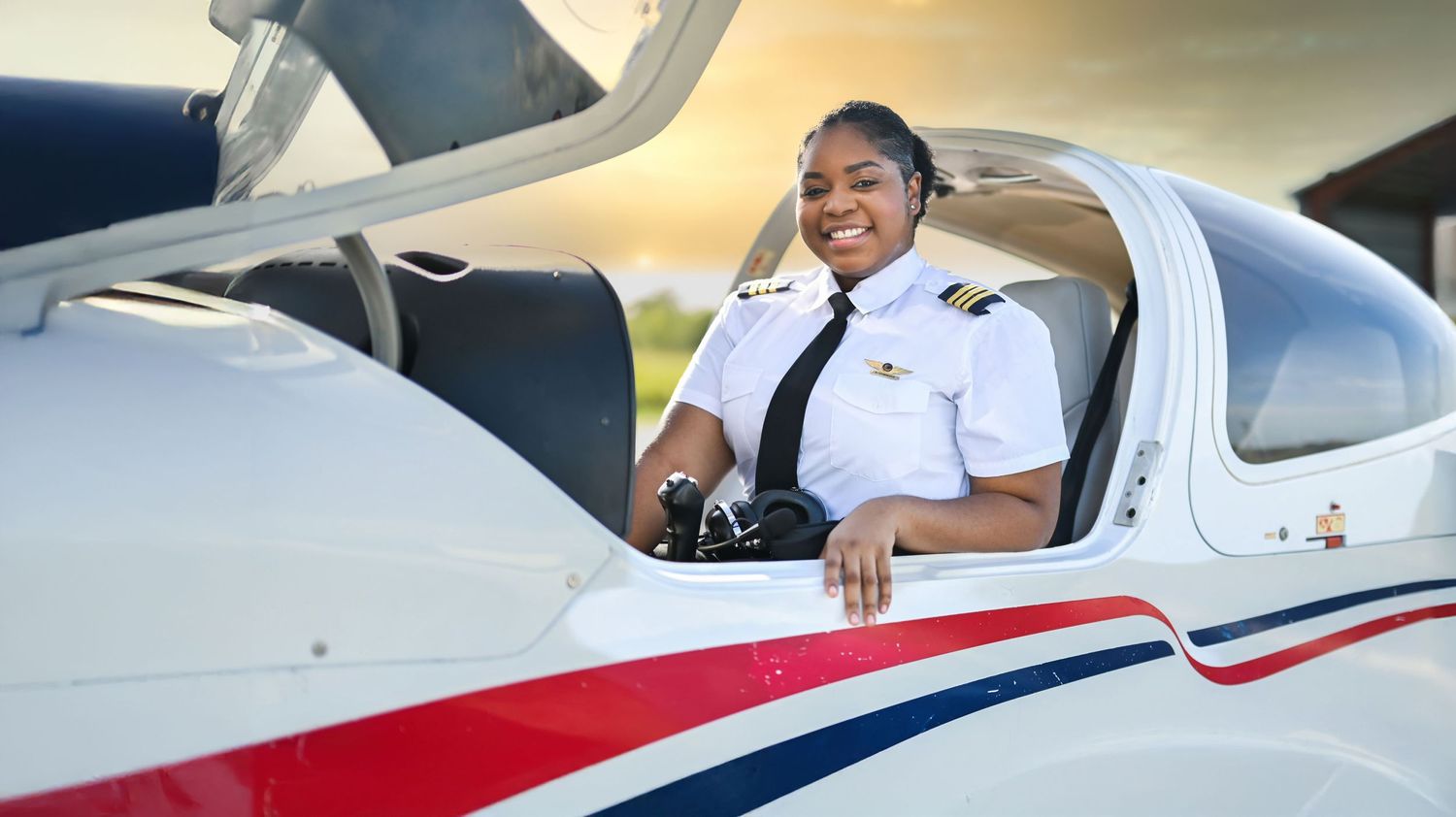 Pilot in white uniform sitting in cockpit of small aircraft with joyful expression.