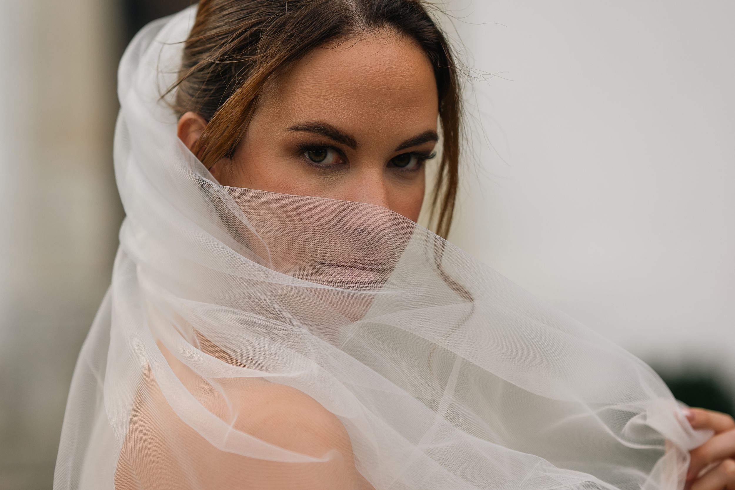 A bride in a flowing white veil looks at the camera with an ethereal, mysterious expression.