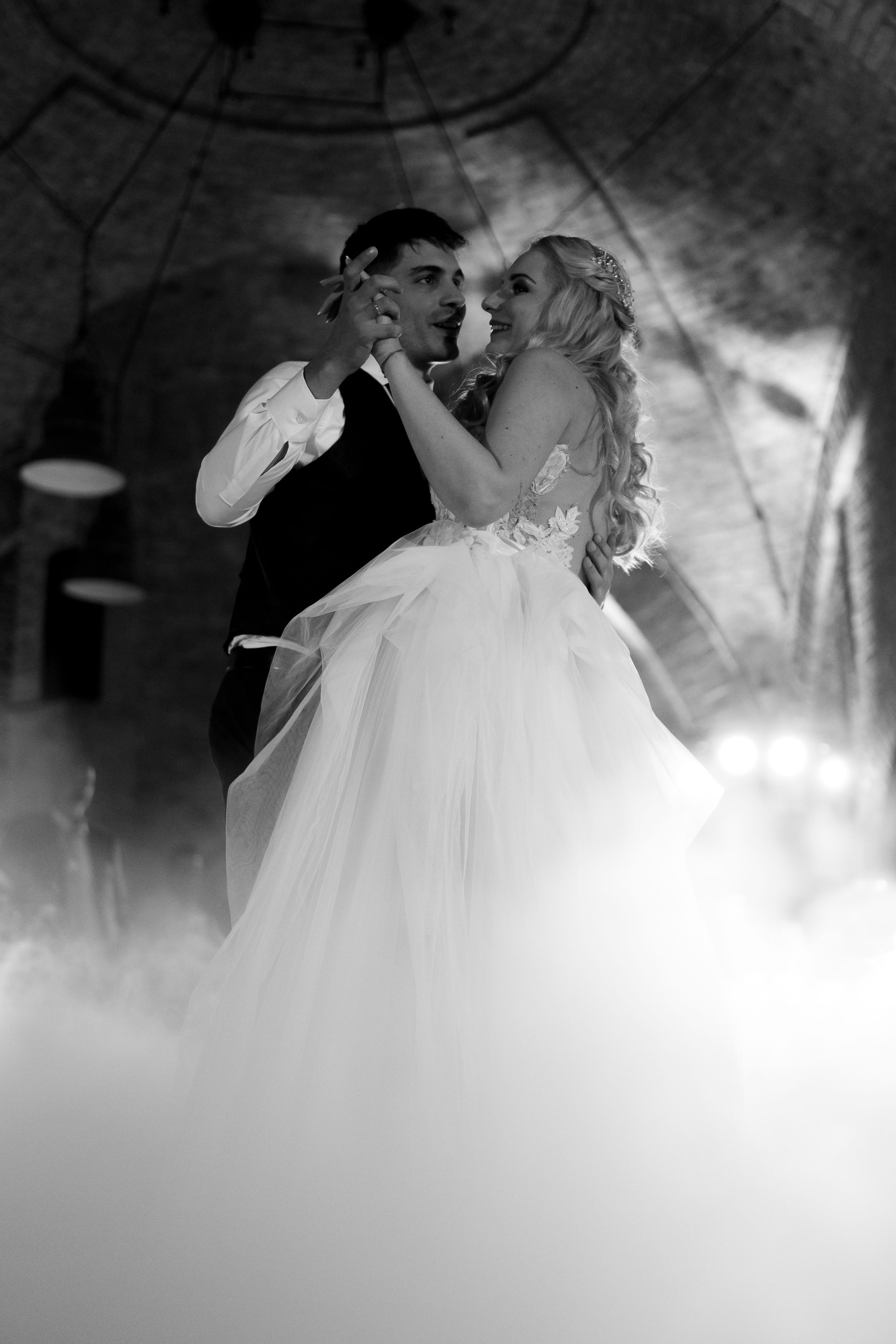 A romantic black and white photograph of a couple dancing on their wedding day amidst dreamy fog.