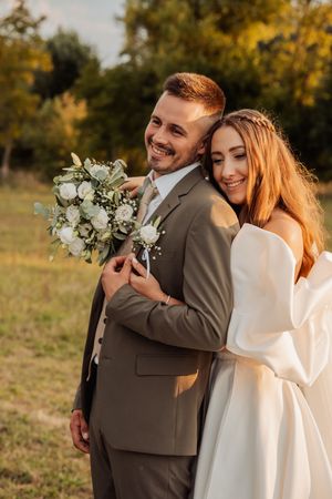 Romantikus esküvői fotózás, amely egy pár gyengéd pillanatait mutatja be napsütötte kültéri környezetben.
