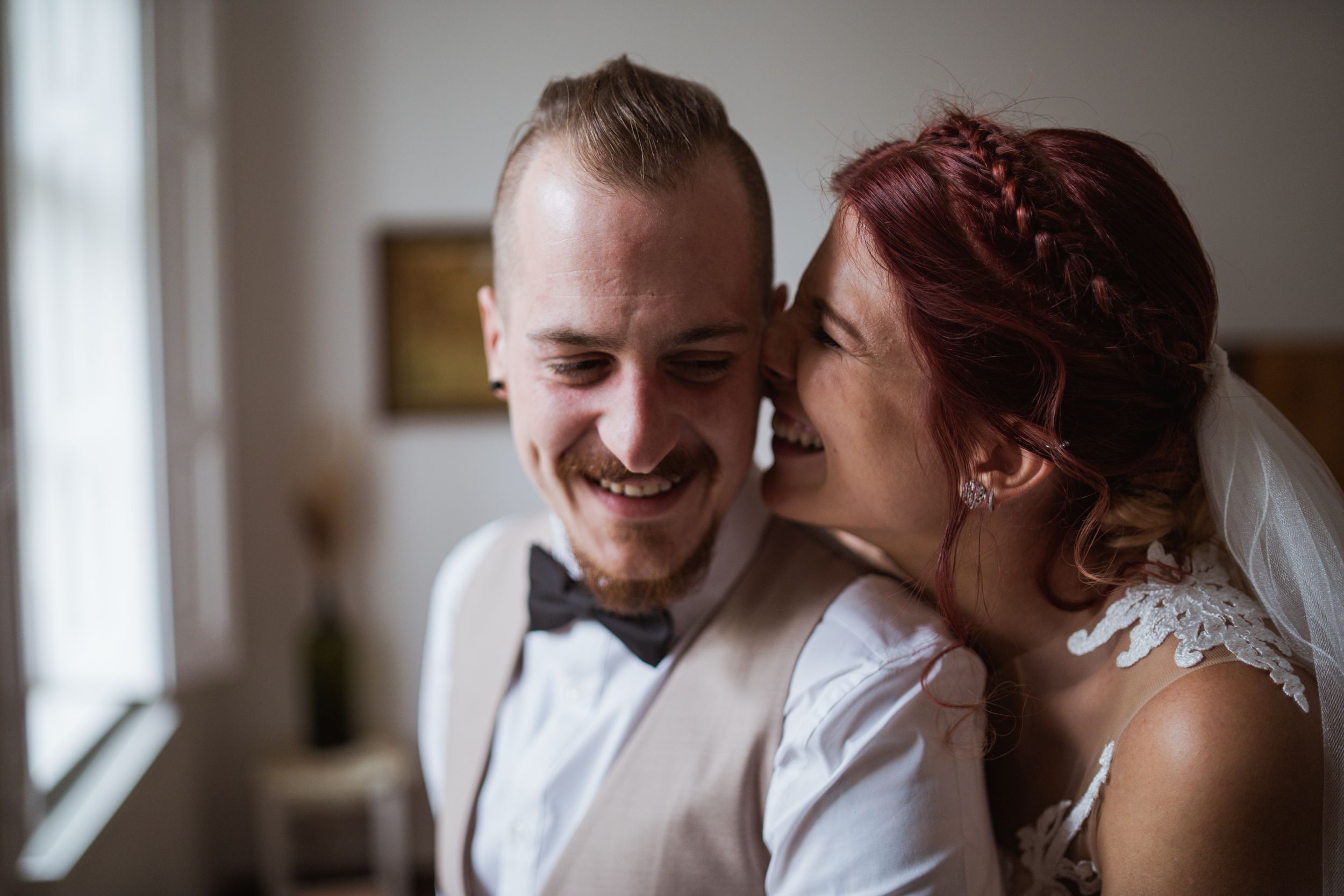 A happy couple shares an intimate moment by a window during their wedding celebration.