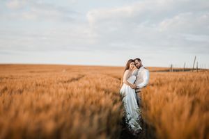 Egy pár szeretettel ölelkezik egy aranyló búzaföldön naplementekor, romantikus sziluettet alkotva a meleg égbolt előtt.