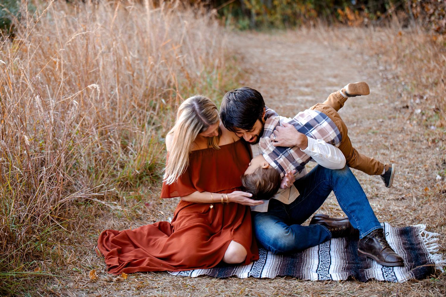 Family relaxing on blanket in rustic setting during fall season.