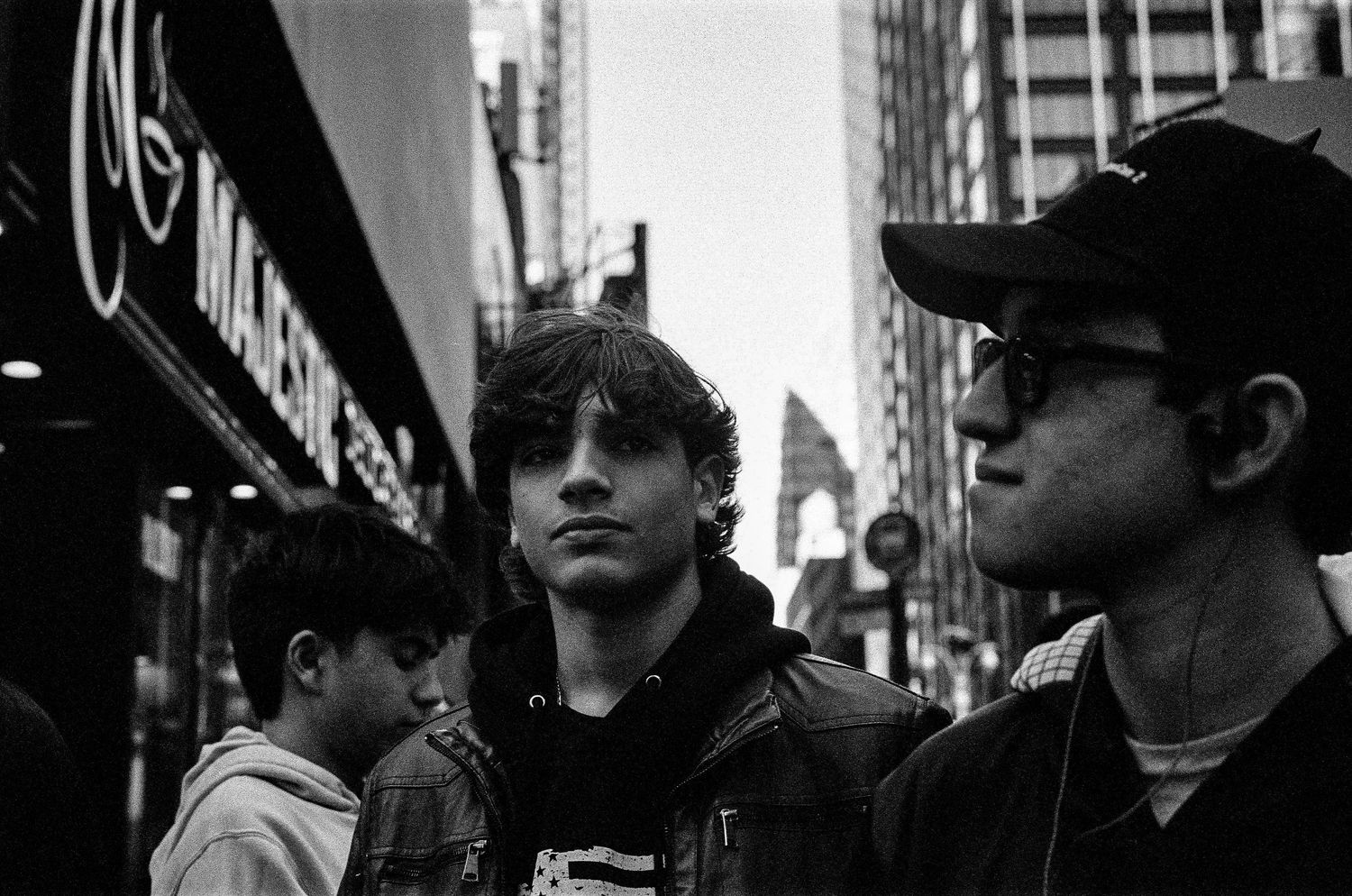Black and white street scene showing people in hoodies and caps walking in an urban setting.