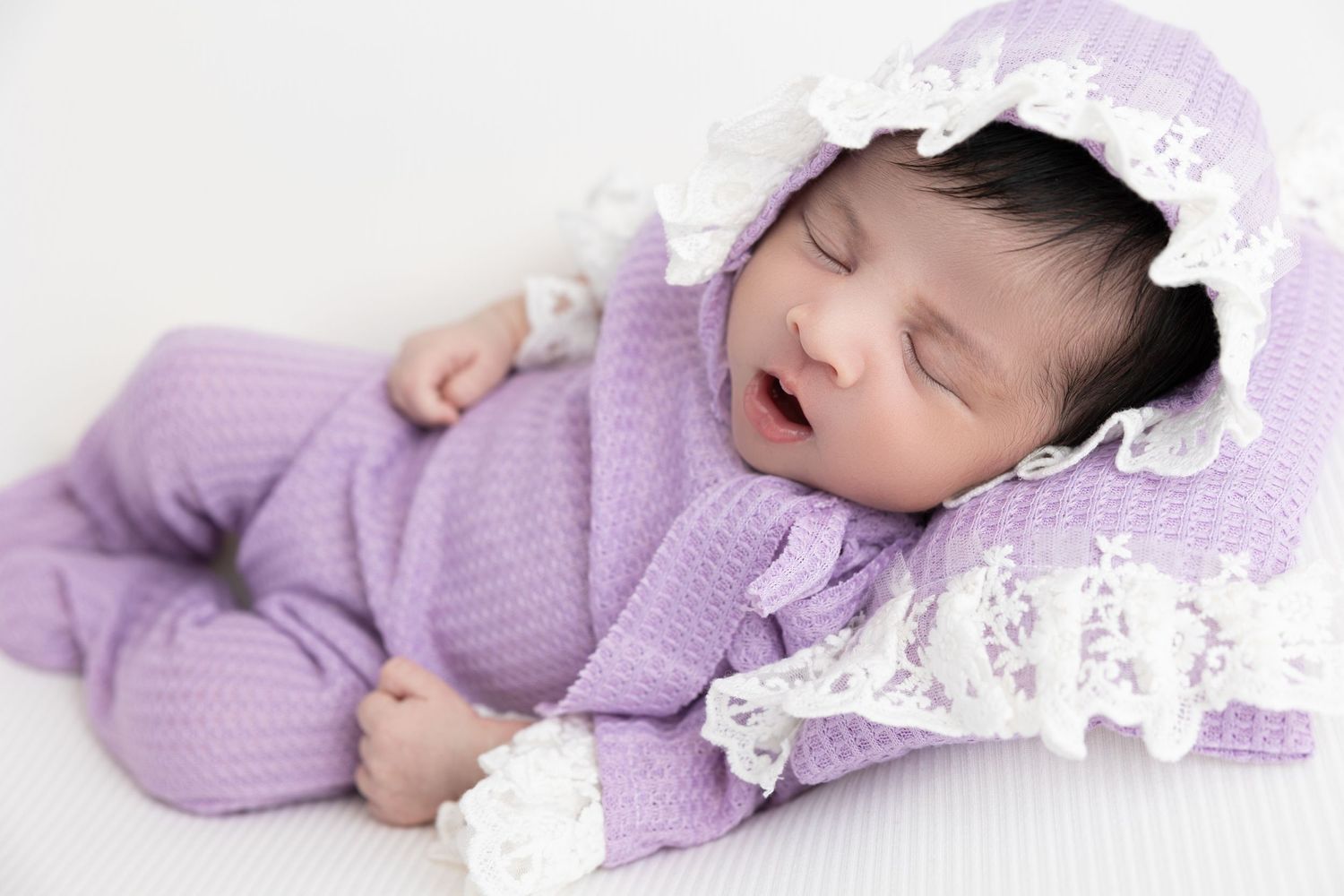 Sleeping baby in lavender knit outfit with lace bonnet.