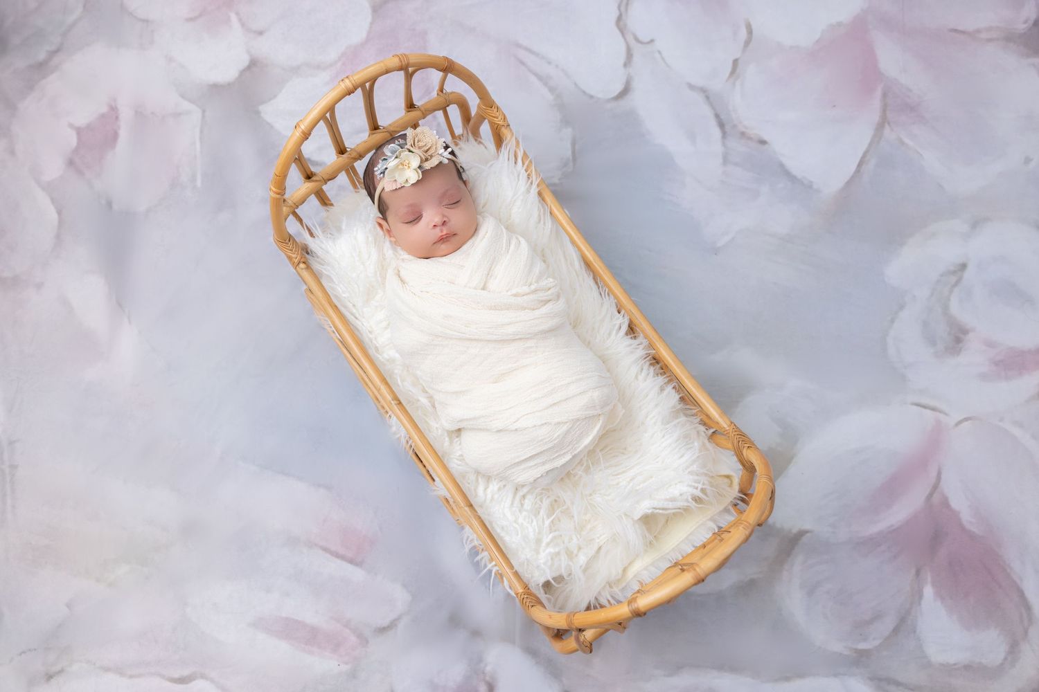 Sleeping newborn wrapped in white swaddle resting in rattan bassinet.