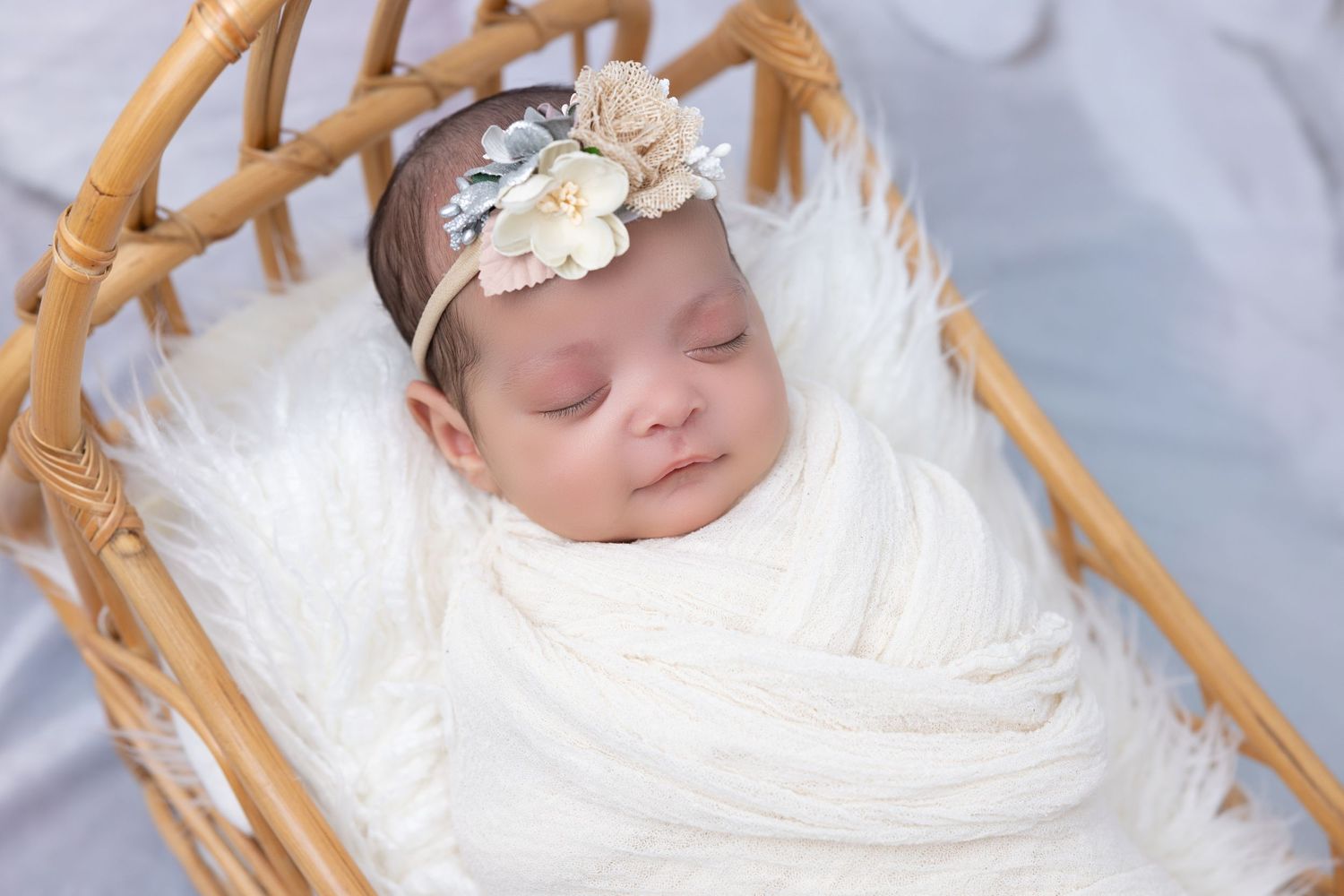 Sleeping baby in white wrap with floral headband in woven bassinet.