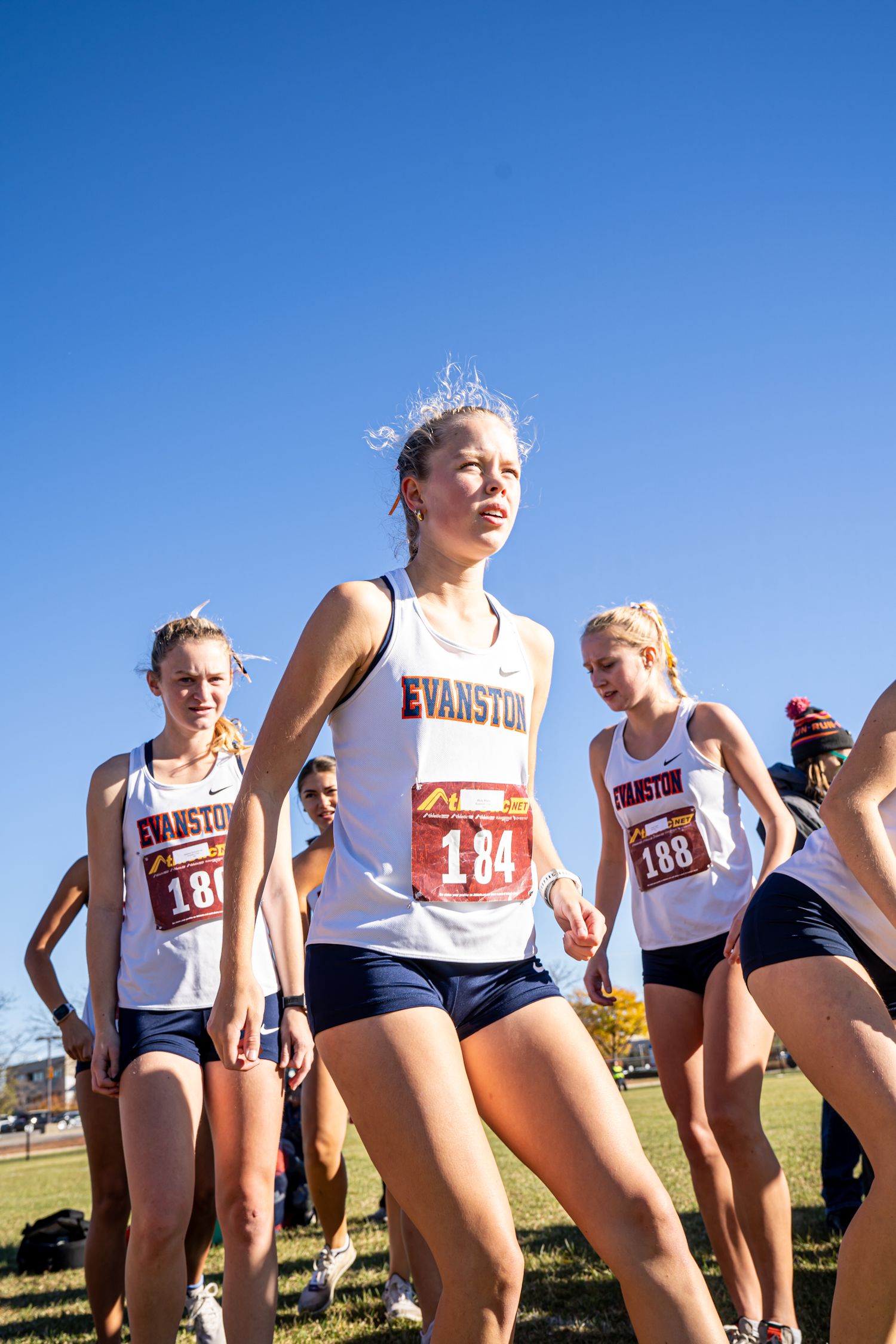 Cross country runners wearing Evanston team uniforms warming up before a race on a sunny day.