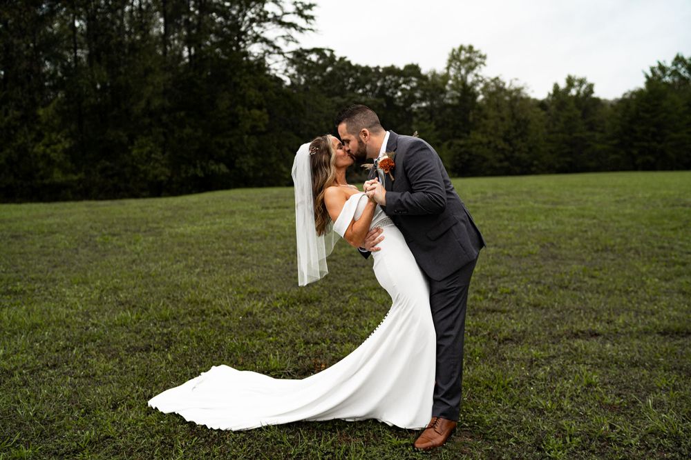 A romantic wedding photo of a couple sharing a sweet moment in an open grassy field.