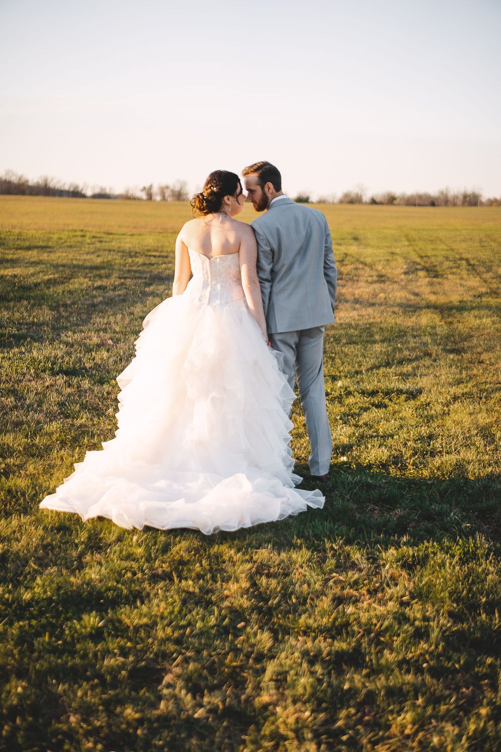 Bride and groom embracing in a sun-lit field during golden hour.