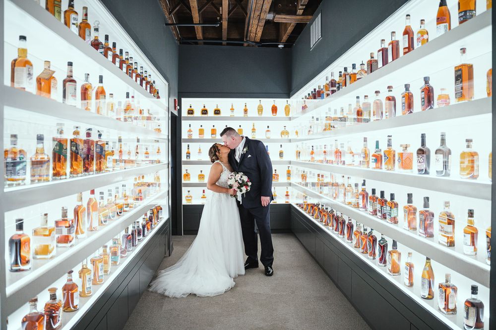 Wedding couple posing in unique whiskey bottle display hallway.