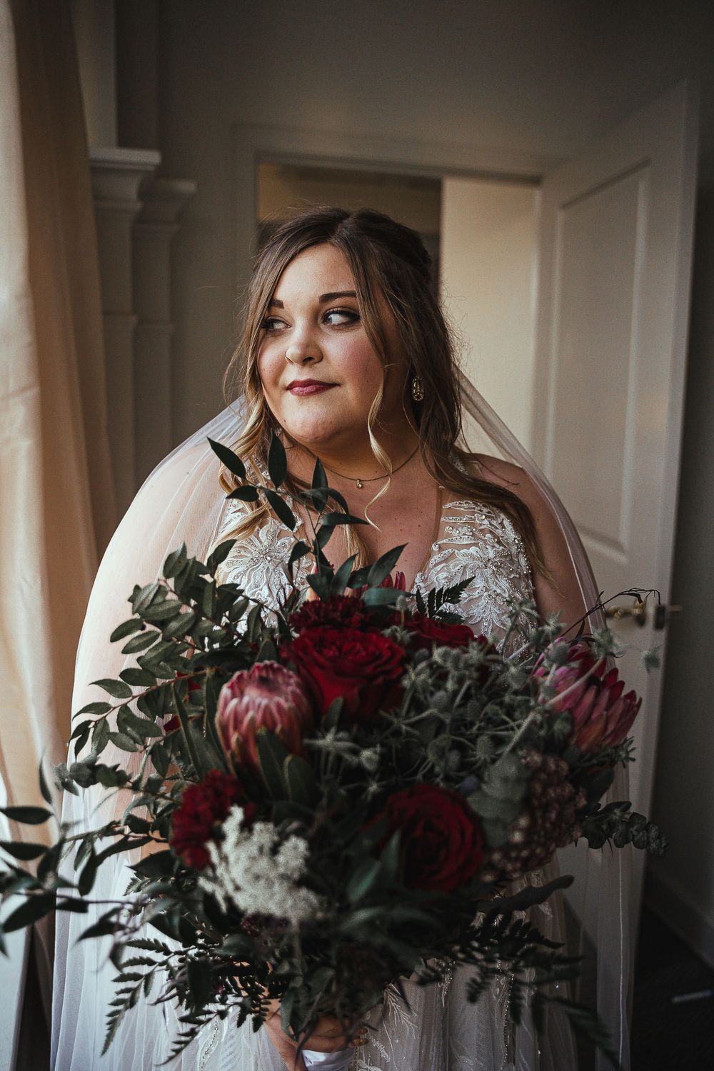 Bride holding a stunning burgundy and green wedding bouquet in natural window light.