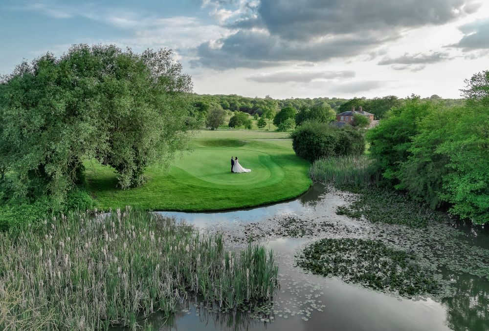 Scenic wedding venue landscape with pond, rolling hills and distant couple silhouette.