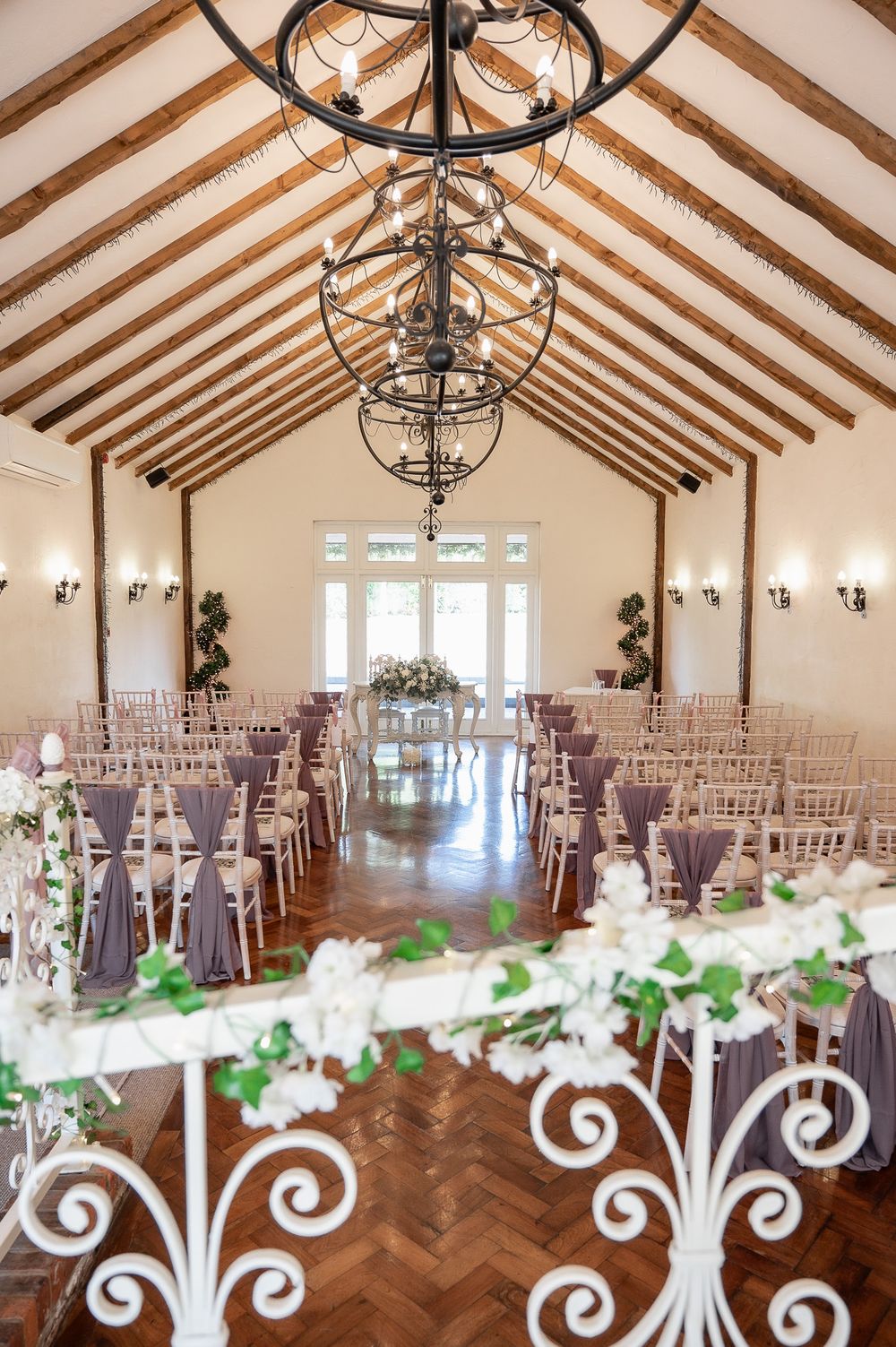 Elegant wedding ceremony venue with vaulted ceiling, chandeliers and purple chair decorations.