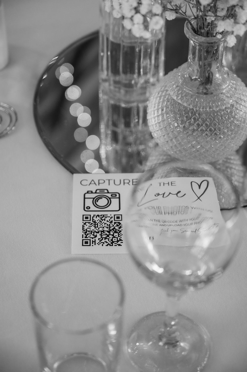 Black and white photo of wedding reception table details with QR code and glassware.