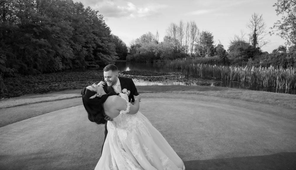 Black and white photo of newlyweds in a dramatic dip pose outdoors.