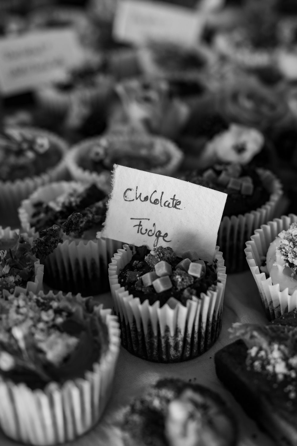 Close-up of chocolate fudge cupcakes with handwritten label at a dessert table.