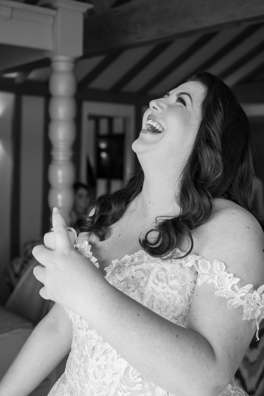 A joyful moment captured in black and white as a bride in a lace dress laughs heartily during her wedding day.