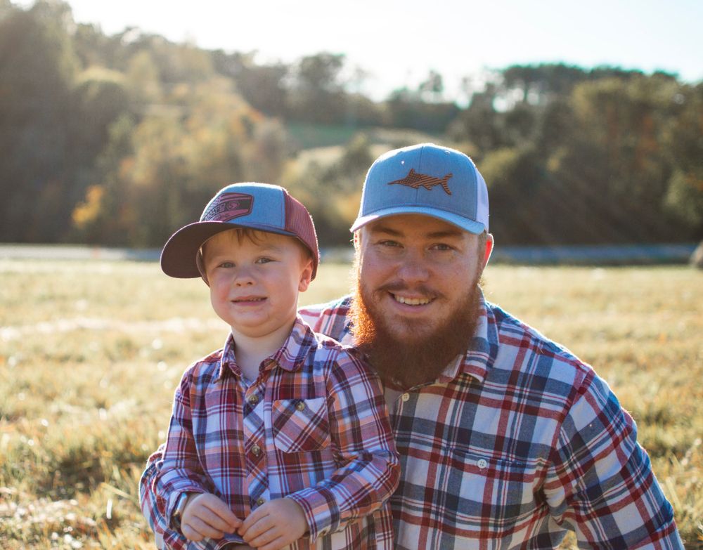 child wearing hat with dad wearing a hat in a grass field