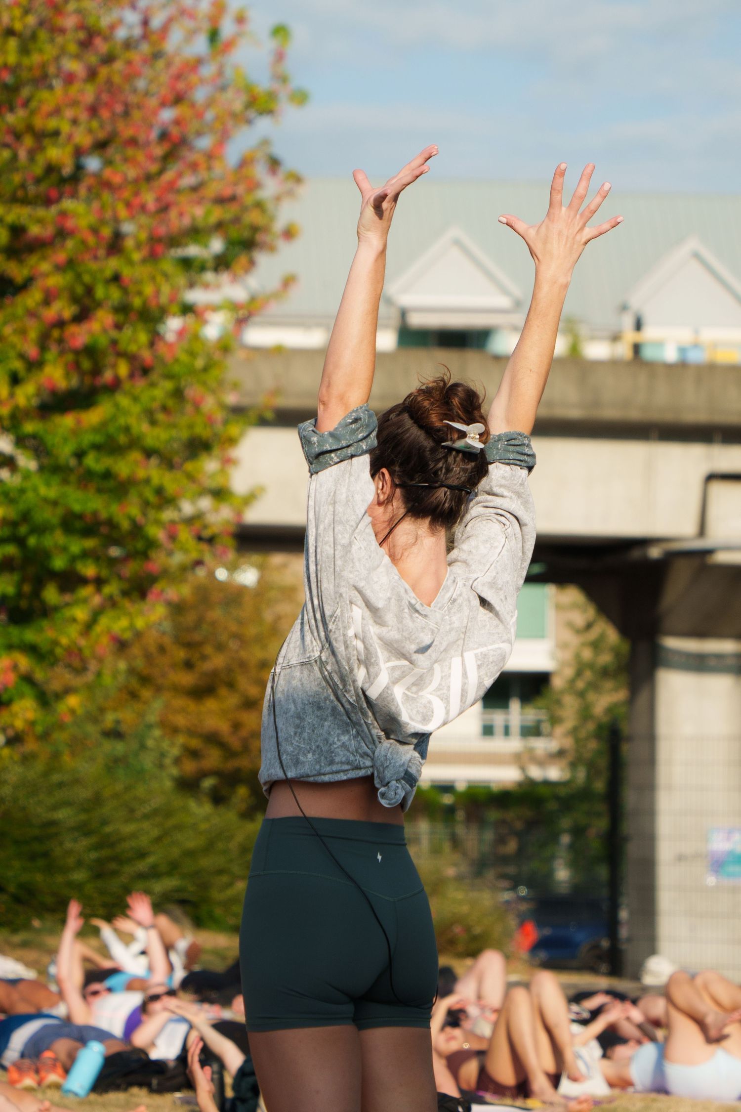 Fitness instructor leading outdoor exercise class with arms raised against autumn backdrop.