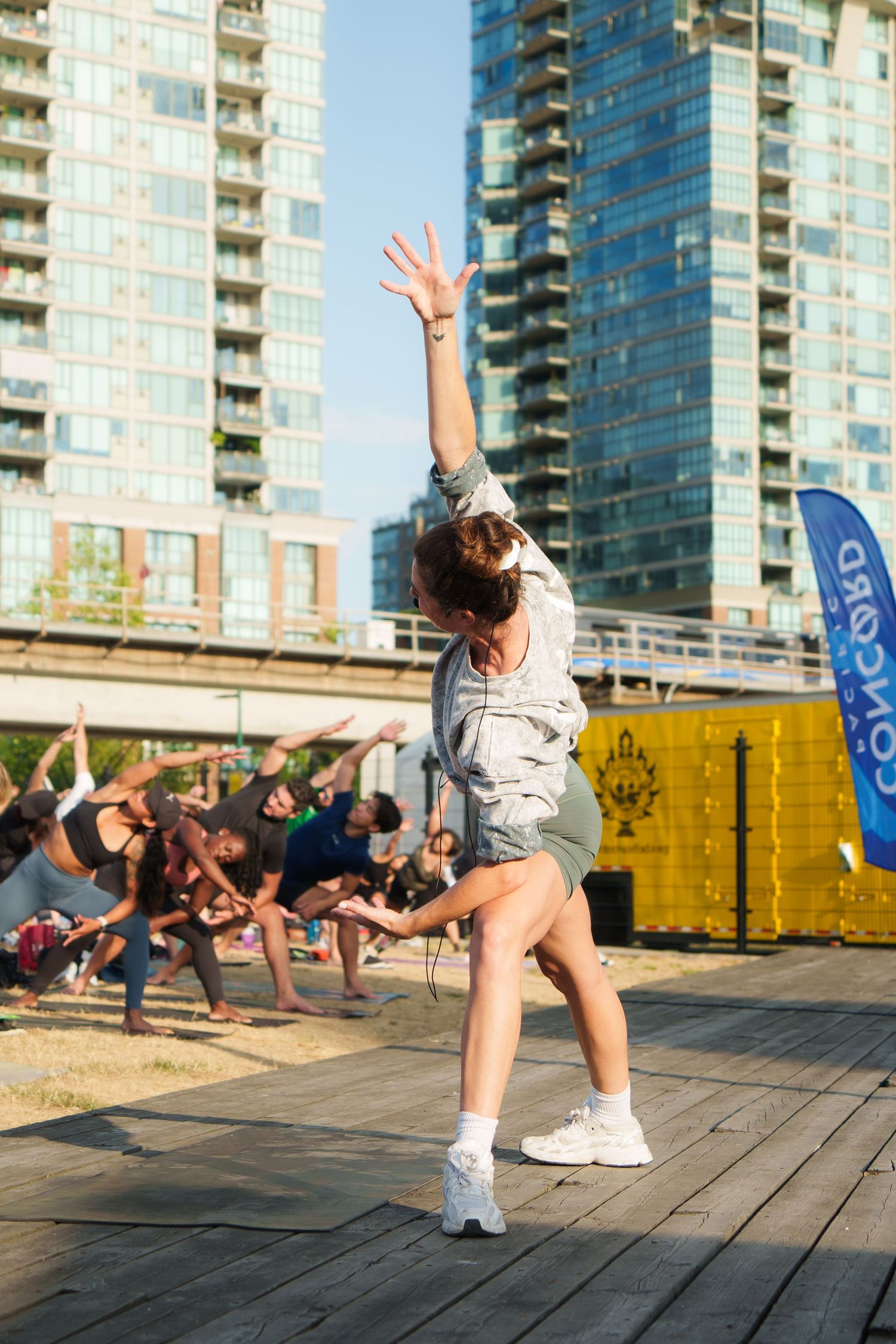 Fitness instructor leading exercise moves on outdoor platform with city skyline background.