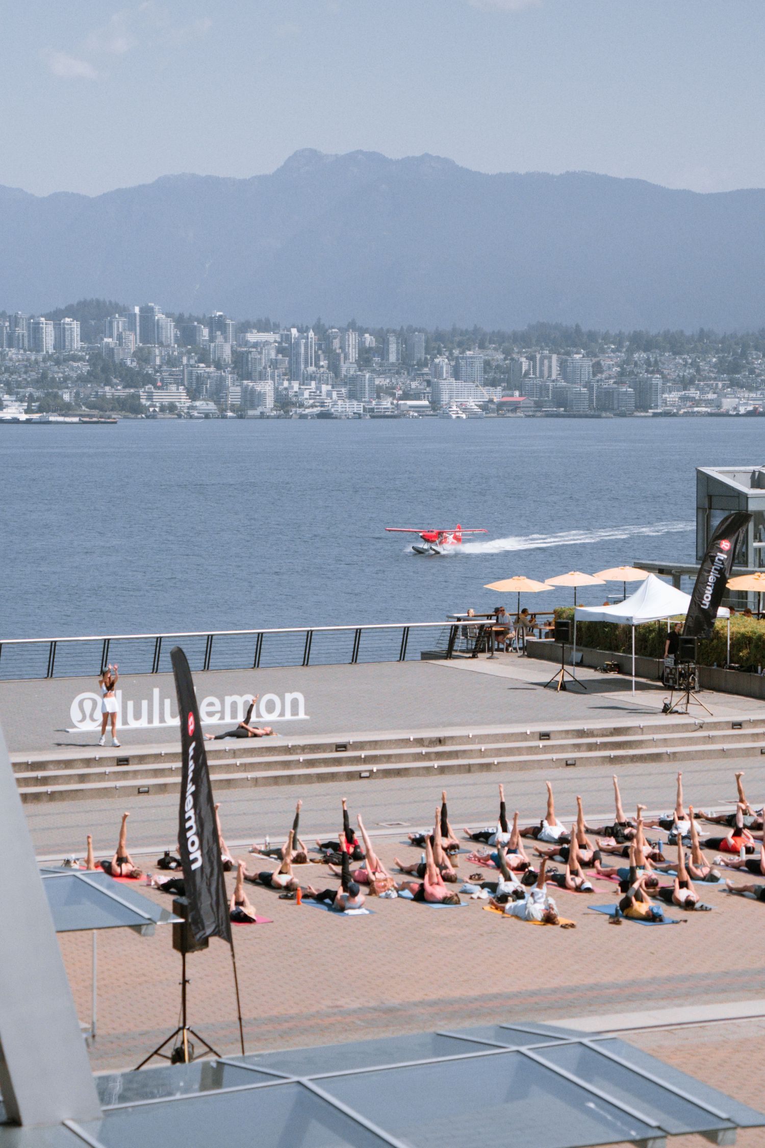 Aerial view of waterfront yoga session with Vancouver skyline and mountains visible.