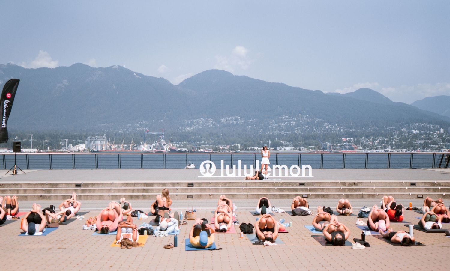 Large outdoor yoga class on Vancouver waterfront with mountains in background.