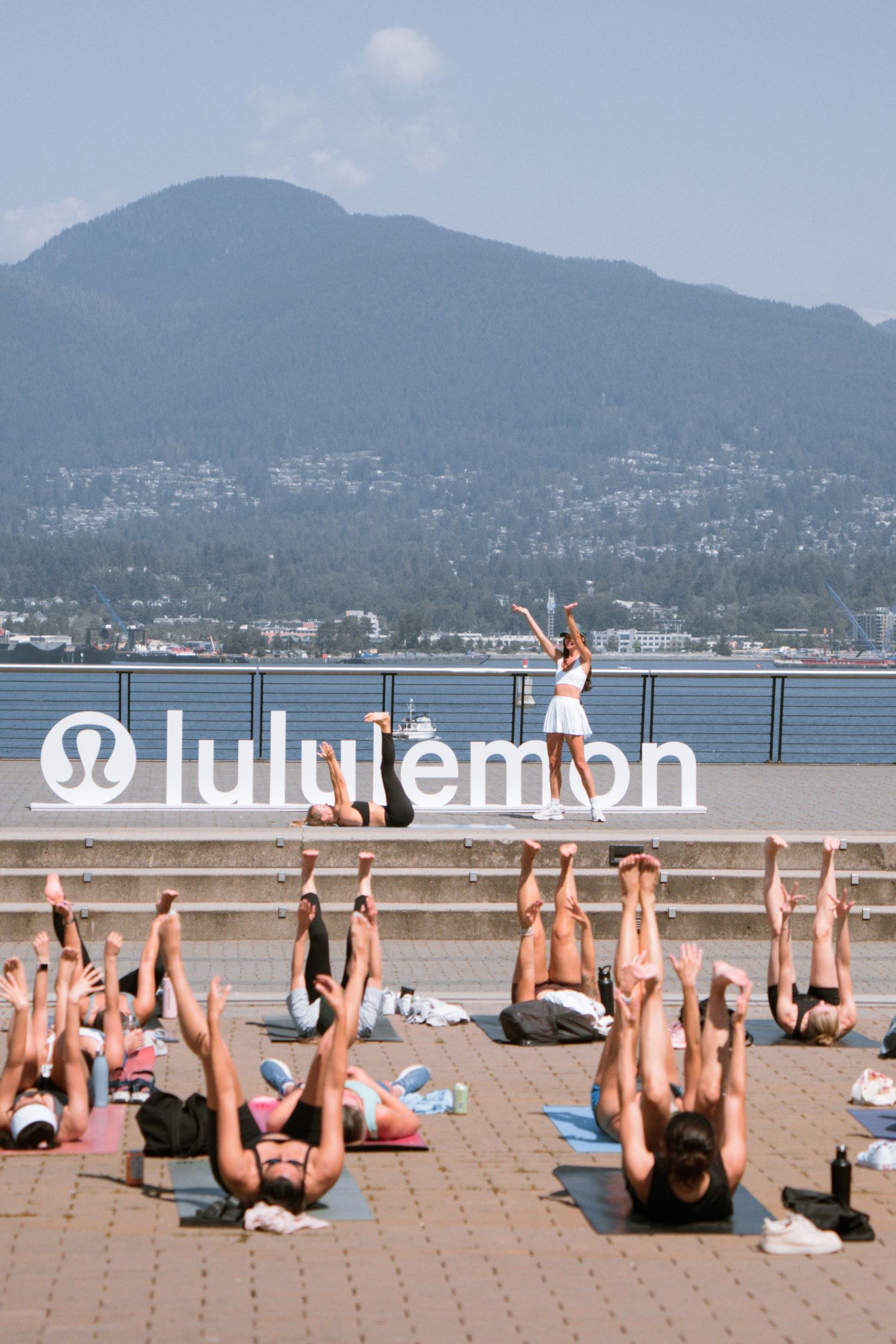Outdoor yoga class stretches in formation by the waterfront with lululemon branding and mountains in background.
