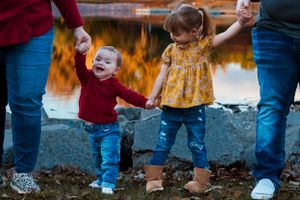 Children holding hands with adults by a reflective pond at sunset.