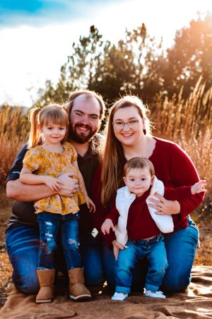 Outdoor family portrait in golden sunlight with tall grass and natural backdrop.
