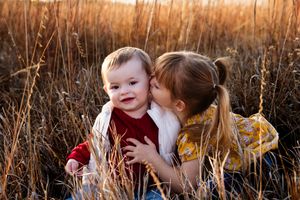 Two children share a sweet moment together in tall golden grass during sunset.