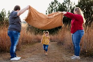 Family plays with a brown blanket on a path surrounded by tall grass.