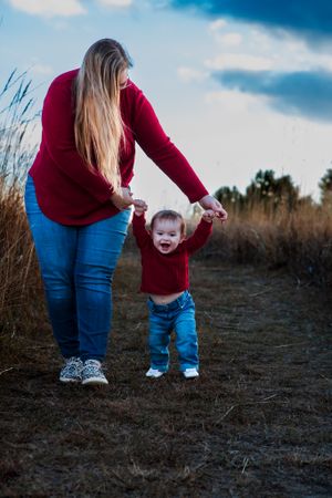 Adult and child walking hand-in-hand on a path through tall grass.