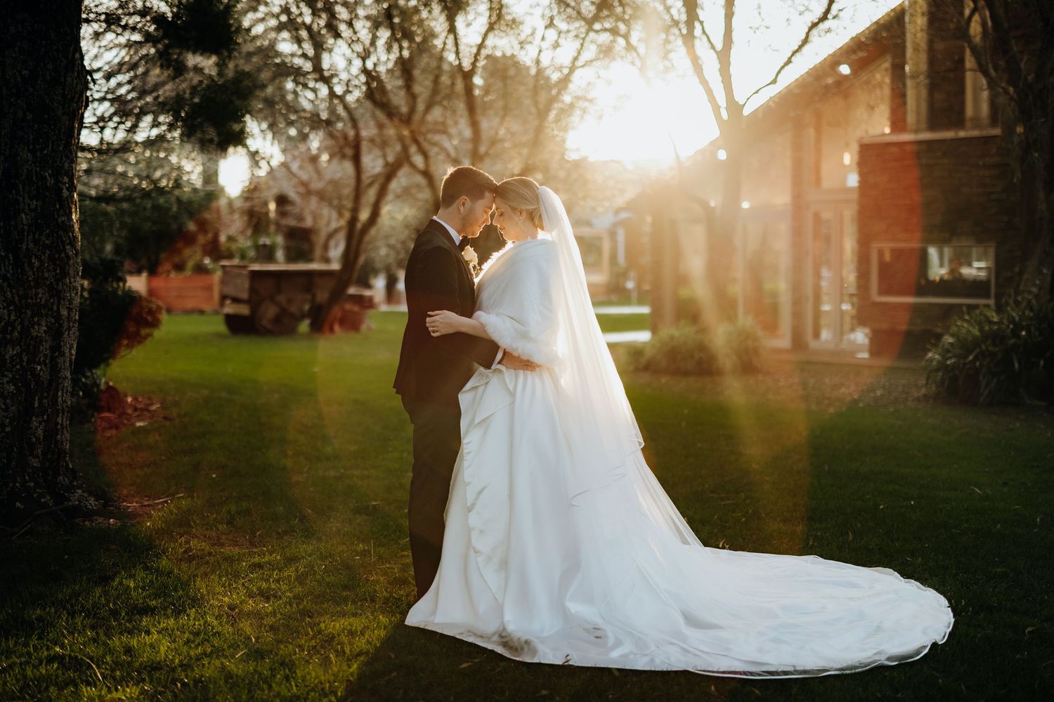 Romantic sunset wedding portrait with couple silhouetted against glowing sunlight.