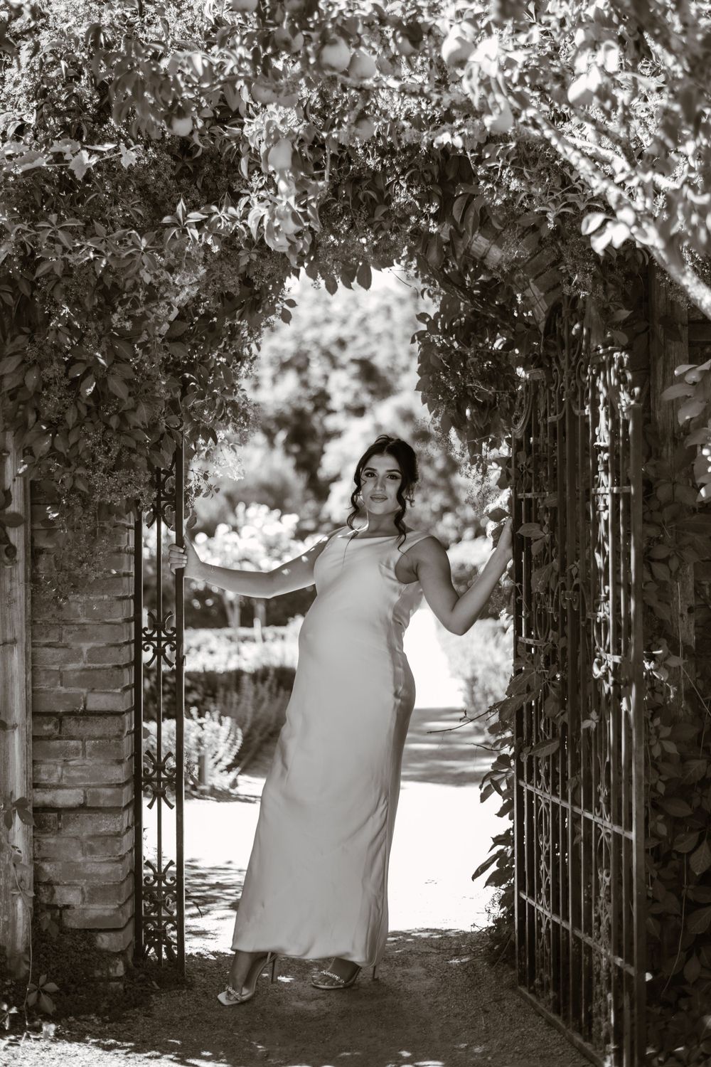 Black and white photograph of a garden entrance with stone pillars and iron gates.