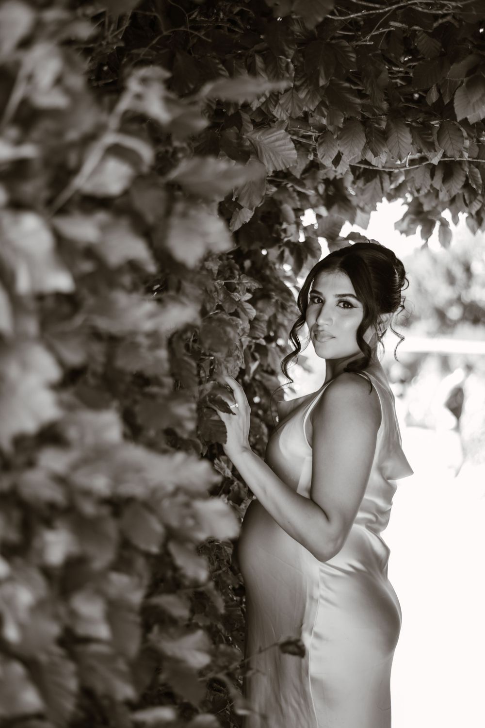 Dreamy black and white portrait among leafy branches in natural light.