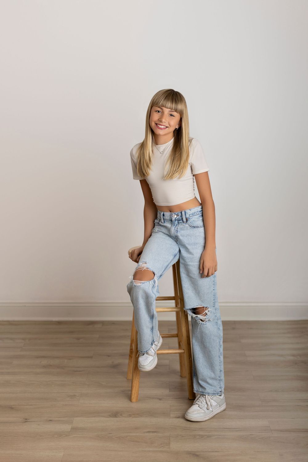 Casual fashion series showing light wash distressed denim jeans paired with white sneakers and crop top on wooden chair.
