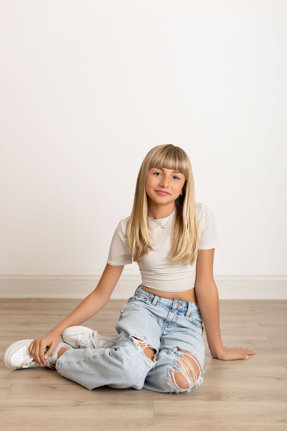 A person in ripped jeans and white top sits casually on hardwood floor in four different relaxed poses.