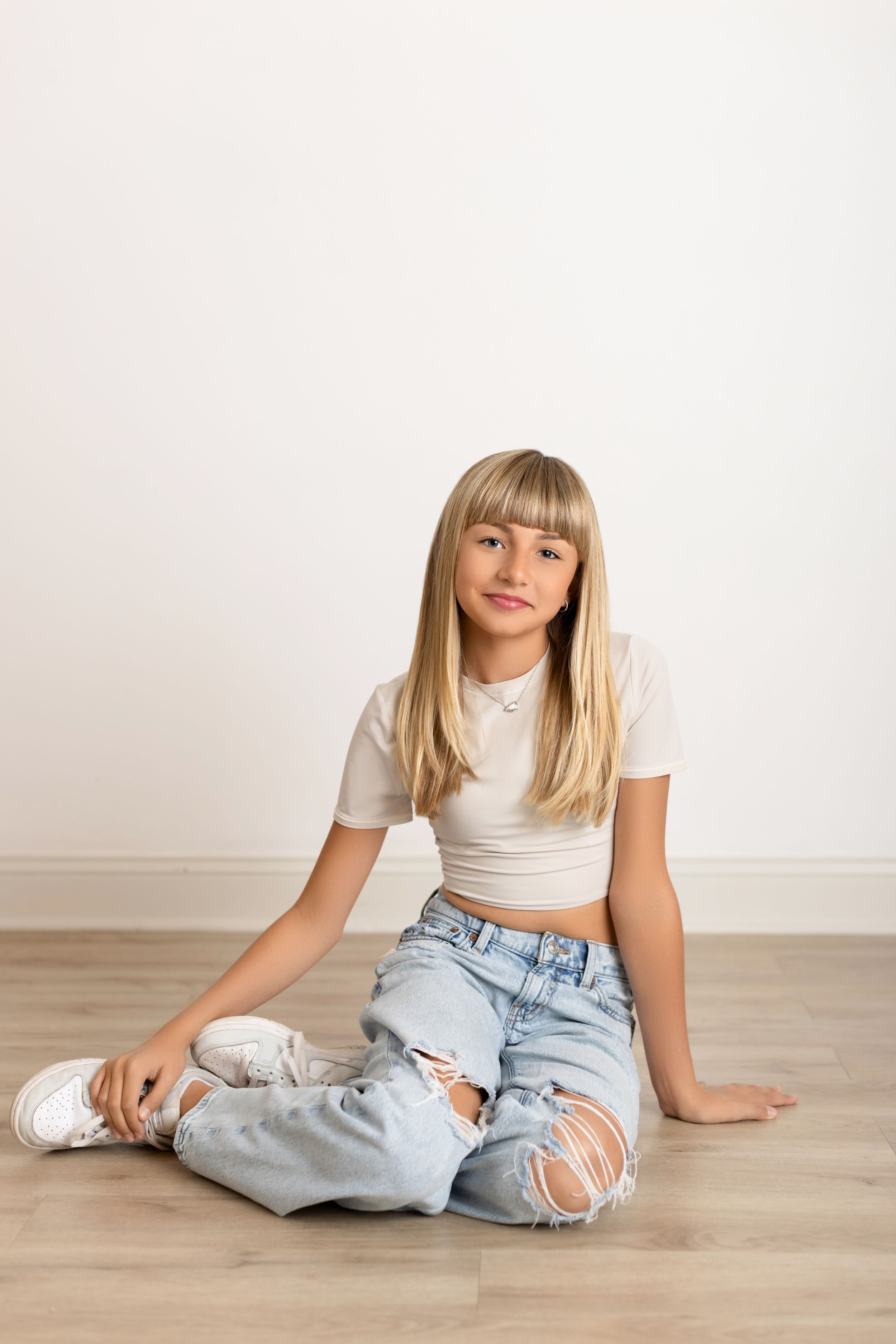 A person in ripped jeans and white top sits casually on hardwood floor in four different relaxed poses.