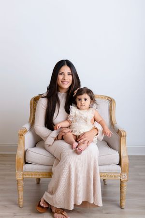 A parent and child in matching pink outfits sit together on an elegant beige French provincial settee.