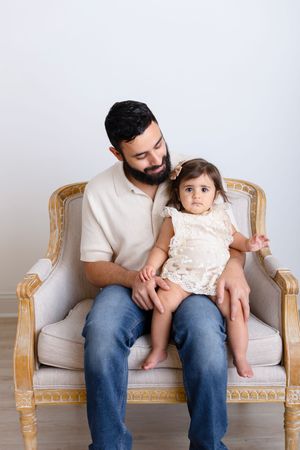 A parent and child share tender moments together on an elegant beige loveseat in a minimalist setting.