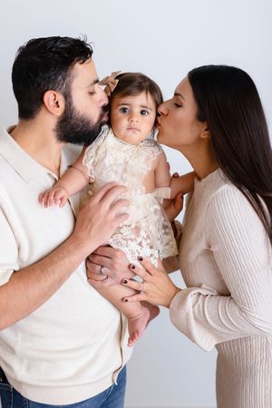 Parents in white and cream outfits share loving kisses with their baby in a sweet photo collage.