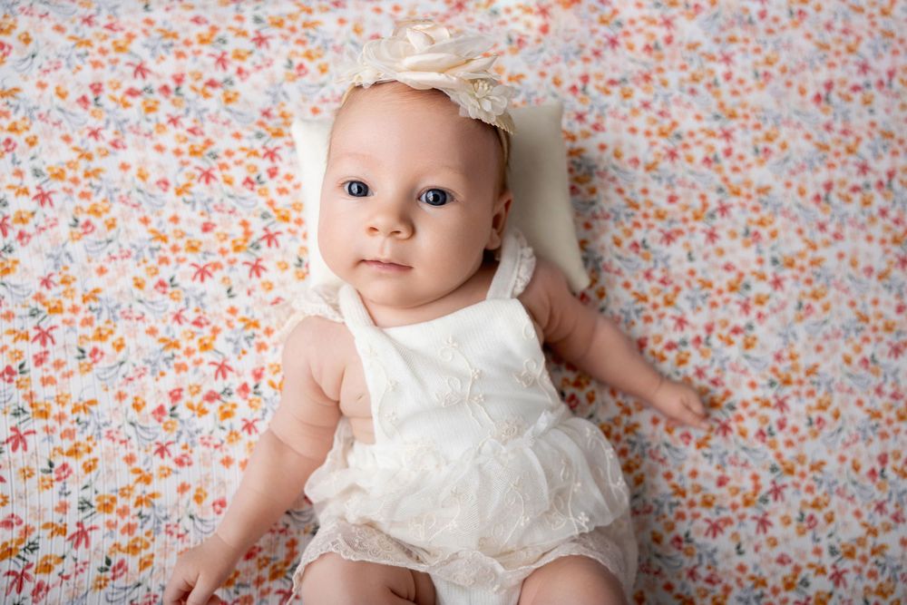 Small baby in white lace romper lying on floral patterned background with soft peachy colors.