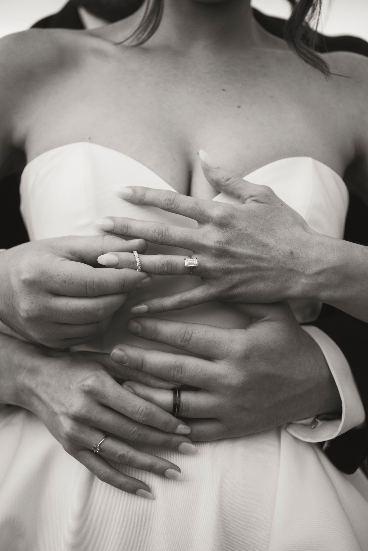 Artistic black and white photo showing hands with wedding rings against white gown.