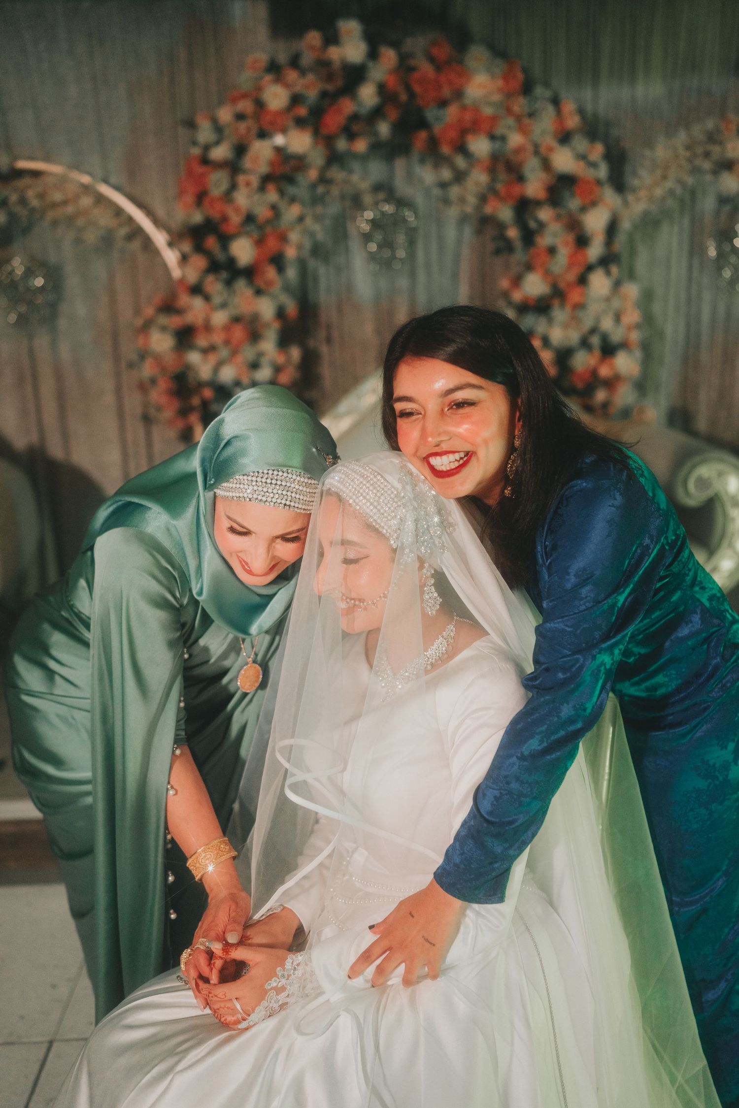 Joyful wedding moment with bridesmaids in jewel-toned dresses helping the bride with wedding preparations.