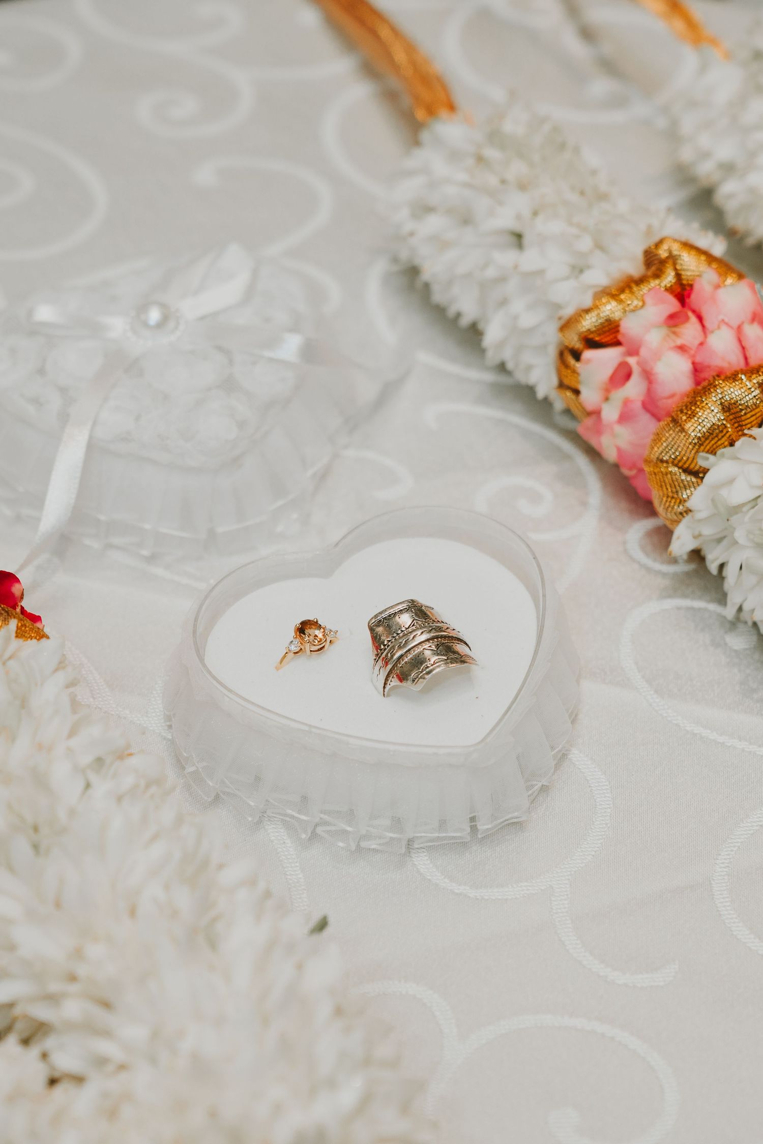 Wedding rings displayed in a heart-shaped container with delicate floral decorations.