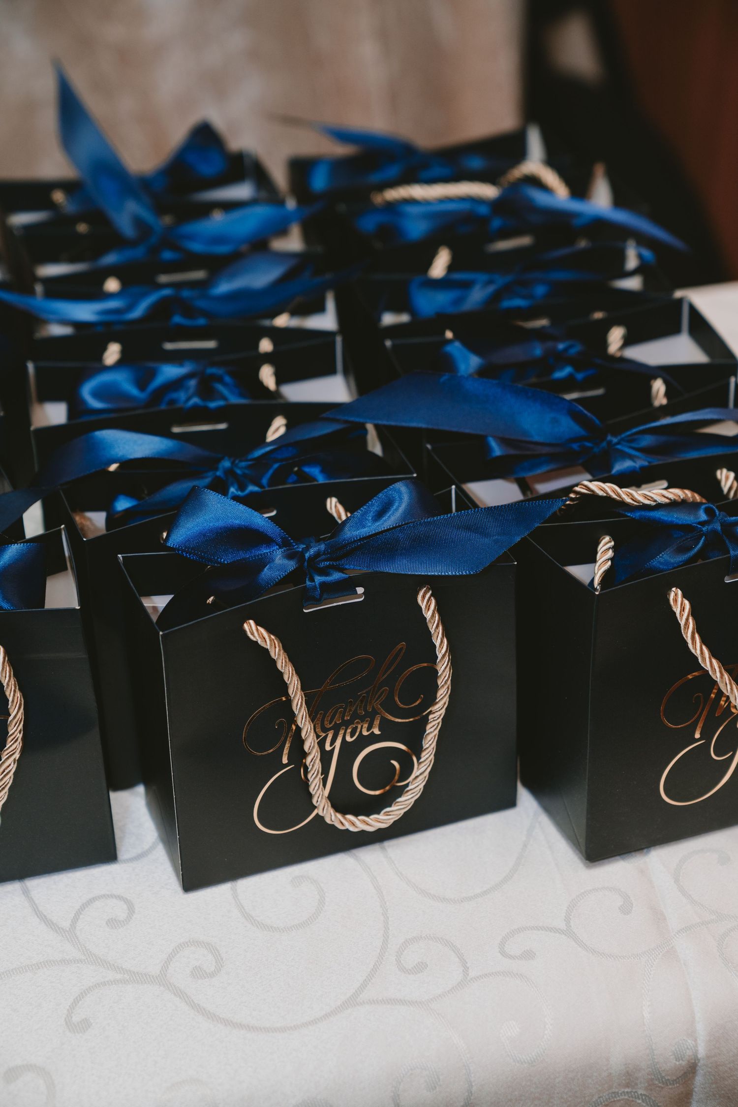 Black gift bags with blue ribbons arranged in rows as wedding favors.