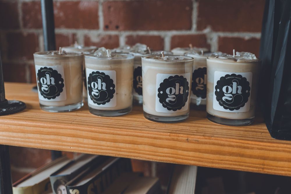 Four "gh" branded soy candles in glass jars displayed on a wooden shelf against a brick wall.