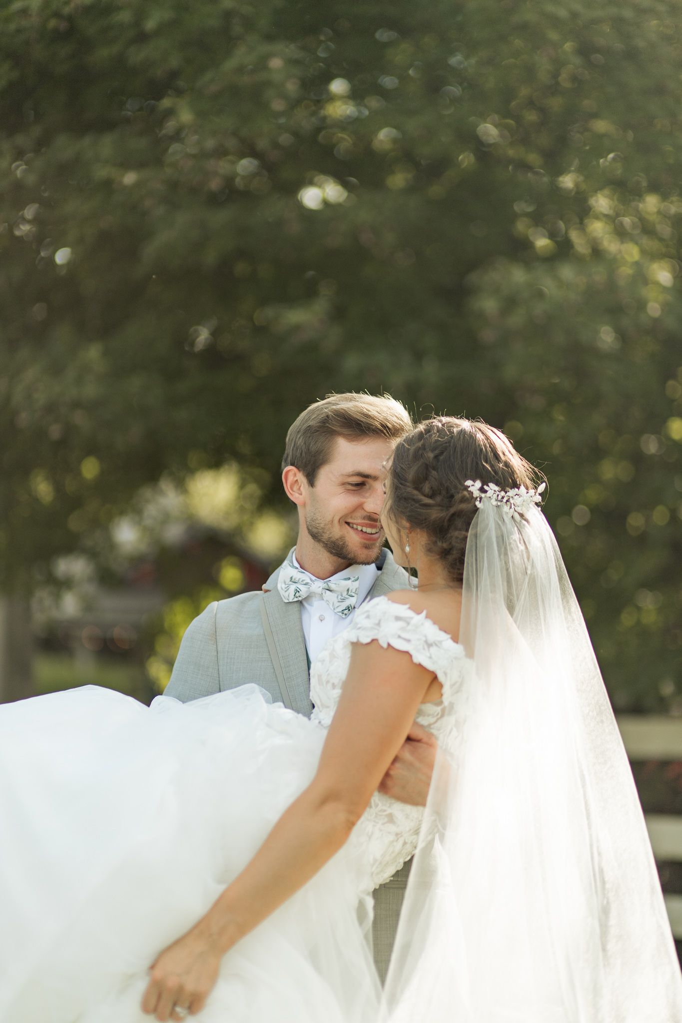 A romantic wedding moment captured in soft sunlight with the bride's veil flowing.