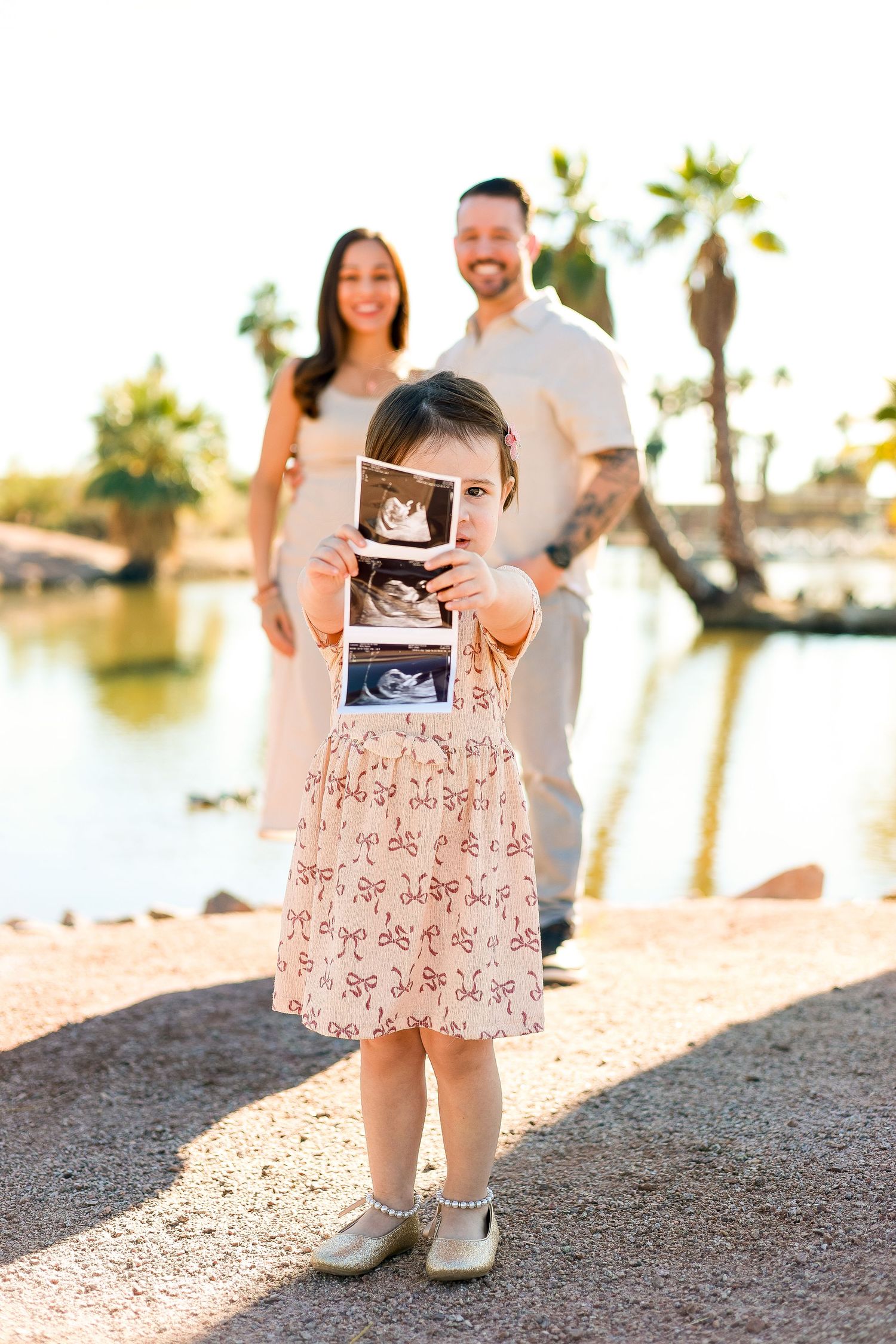 A couple holds up ultrasound photos during a pregnancy announcement photoshoot at sunset on a beach.